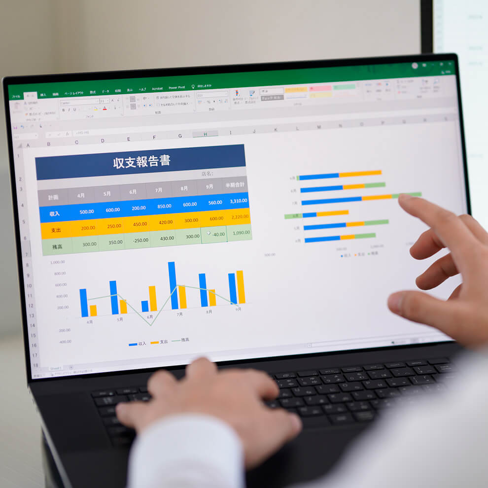 Excelの画面が表示されたノートパソコンと操作する手